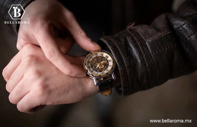 Dos brazos que lucen la manga de una chamarra de piel café mientras ajusta el reloj análogo que se encuentra en la muñeca izquierda