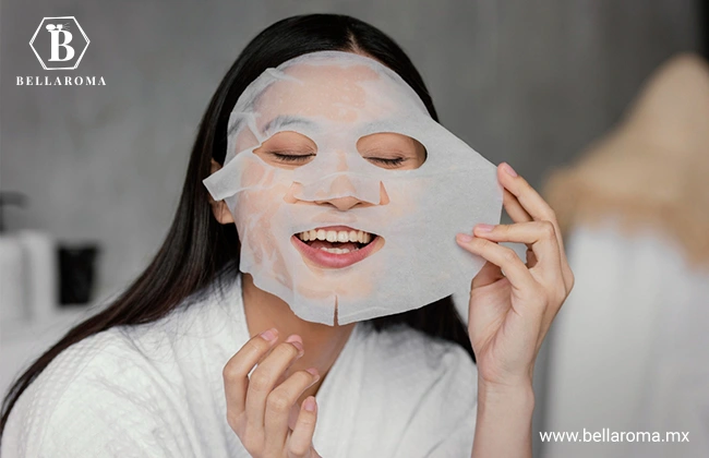 Mujer en bata de dormir quitándose de la cara una mascarilla de skincare.