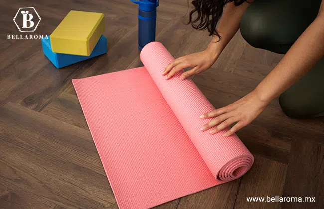 Mujer en cuclillas enrollando un tapete de yoga color rosa. Este es uno de los productos en tendencia para vender por mayoreo