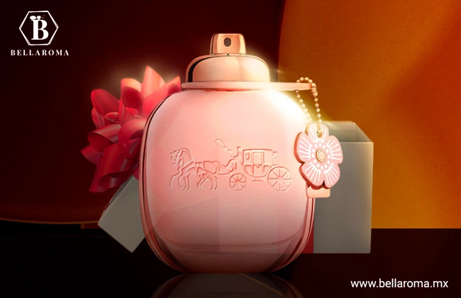 Perfume Coach de frasco rosa con detalle de relieve en forma de caballo y carruaje, y accesorio de flor rosa, sobre base oscura y fondo naranja.