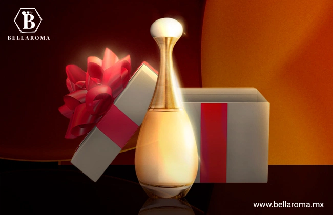 Perfume Jadore de Christian Dior, color dorado y amarillo, en frente de caja de regalo con moño rojo.