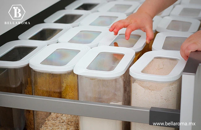 Contenedores de plástico transparentes con tapas blancas organizados dentro de un cajón de cocina para el almacenamiento de alimentos.