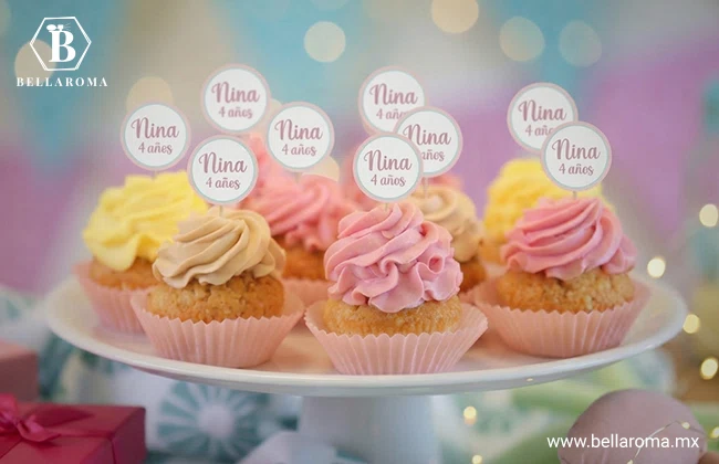 Muffins y cupcakes infantiles decorados con betún rosa y amarillo sobre una base blanca de repostería para eventos.