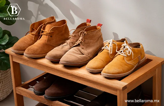 Tres pares de botas y zapatos casuales de gamuza en tonos café y mostaza ordenados en un zapatero de madera.